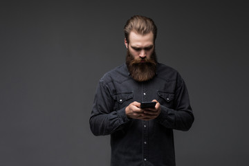 Portrait of a handsome attractive long bearded man holding mobile phone isolated on gray background