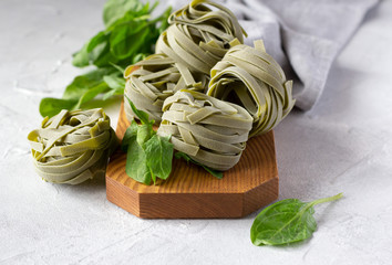 Uncooked spinach pasta tagliatelle (agli spinaci) with fresh spinach leaves on wooden board