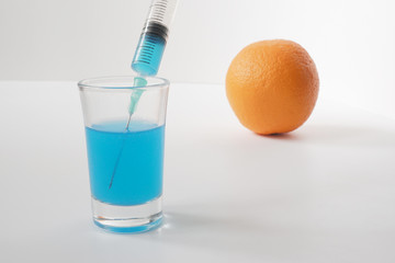 Injecting blue liquid into an orange fruit. Syringe with blue liquid on the white background.