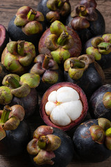 ripe mangosteen fruits and cross section showing the thick violet skin and white flesh, Queen of fruit on wooden background.