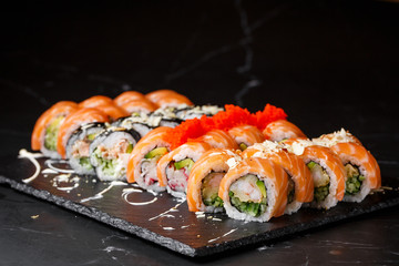 Various kinds of sushi served on black marble background. Sushi menu for Japanese food. Japanese sushi set. Rolls with tuna, salmon, shrimp, crab, caviar and avocado. Horizontal photo.