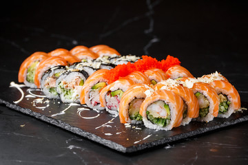 Various kinds of sushi served on black marble background. Sushi menu for Japanese food. Japanese sushi set. Rolls with tuna, salmon, shrimp, crab, caviar and avocado. Horizontal photo.