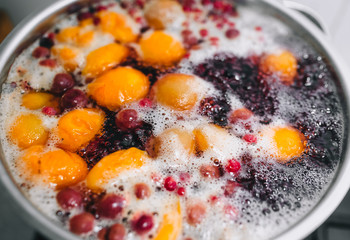 Fresh fruits: apricots, cherries, raspberries, apples are boiled in boiling water in a metal pan on a stove with bubbles and foam close-up. Cooking delicious homemade compote. Photography, concept.