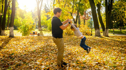 Young man playing and havng fun with his little son in autumn park