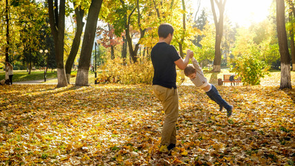Young father holding his son by hands and spinning in autumn park