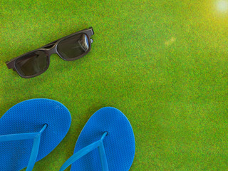 Summer vacation concept in sunshine. a sunglasses and blue flip-flops on green grass background