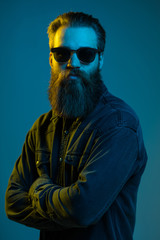 Young bearded man wear in sunglasses with crossed hands isolated on light background.