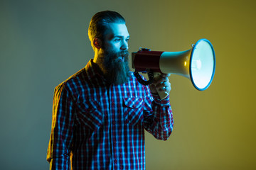 Young hipster man shouting by megaphone isolated on yellow background