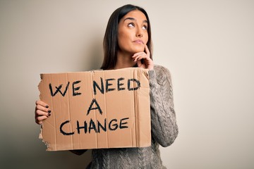 Young beautiful brunette activist woman protesting for a change holding banner serious face...