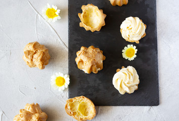 Cream puffs or profiteroles with whipped cream and halves  on slate board, small white and yellow flowers. Top view