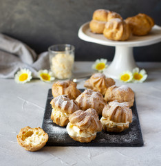 Cream puffs or profiteroles with whipped cream dusted with sugar powder on slate board, classic French dessert