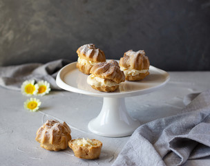 Cream puffs or profiteroles filled with whipped cream dusted with sugar powder on cake stand, classic French dessert