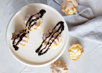 Cream puffs or profiteroles filled with whipped cream dusted with sugar powder and garnished with chocolate sauce on cake stand. Top view