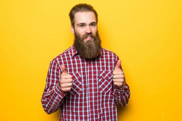 Fototapeta premium Young bearded man with thumbs up on yellow background