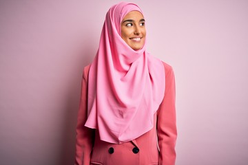 Young beautiful brunette businesswoman wearing pink muslim hijab and business jacket looking away to side with smile on face, natural expression. Laughing confident.