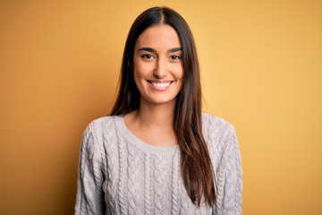 Young beautiful brunette woman wearing white casual sweater over yellow background with a happy and cool smile on face. Lucky person.