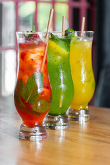Three glass with strawberry and classic mojito cocktail with lemon and mint, cold refreshing drink or beverage with ice on bright background. Overhead view, copy space. Advertising for cafe menu