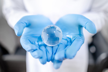 Global health and medicine. Heal the world concept. Doctor, nurse or medical worker in white protective suit with blue sterile rubber gloves holding world globe crystal glass ball in hand.