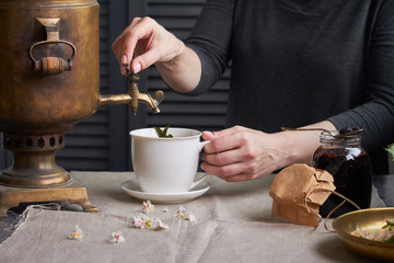 Side view of female hands pouring cup of tea from vintage samovar and jar of homemade jam, tea...