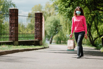 Woman in protective face mask with goods after shopping. a walk in the park after quarantine