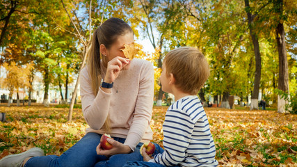Beautiful young woman looking through yellow autumn leaf at her son in autumn park