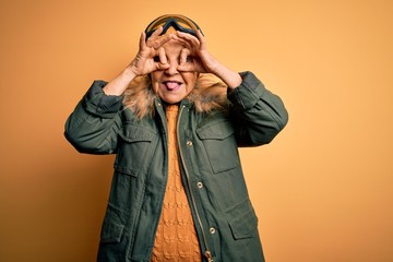 Senior beautiful grey-haired skier woman wearing snow sportswear and ski goggles doing ok gesture...