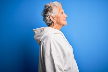 Senior beautiful sporty woman wearing white sweatshirt over isolated blue background looking to...