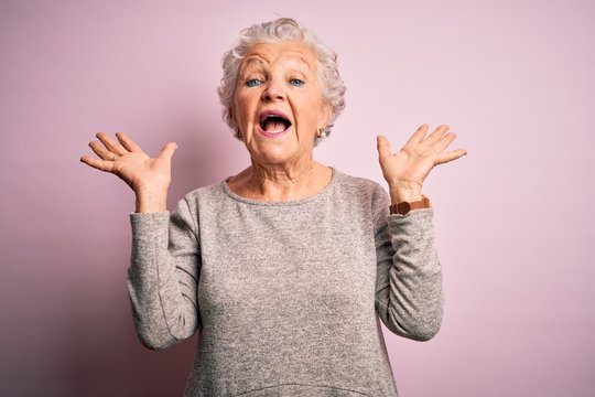 Senior beautiful woman wearing casual t-shirt standing over isolated pink background celebrating crazy and amazed for success with arms raised and open eyes screaming excited. Winner concept