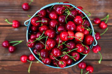 Fresh red ripe cherry in a bucket on the wooden background, top view. Ripe red cherries in the metal bucket on a wooden background