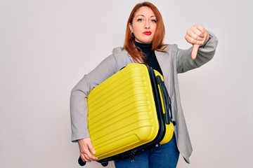 Young beautiful redhead woman holding suitcase prepared to business travel with angry face, negative sign showing dislike with thumbs down, rejection concept