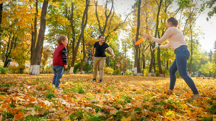 Naklejka na ściany i meble Happy young parents playing with their little son in frisbee at autumn park
