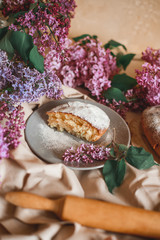 Homemade Apple pie on a wooden table next to a bowl of lilacs. Gentle toning.
