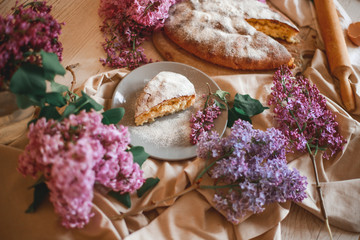 Homemade Apple pie on a wooden table next to a bowl of lilacs. Gentle toning.