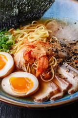 Asian noodle soup, ramen with pork, tofu, kimchi, vegetables and egg in blue bowl. Slate background. Top view. Bowl of asian style soup. Japanese cuisine. Top view. Banner. Asian food