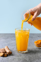 Pouring golden turmeric iced latte. Ayurvedic drink on light blue background. Vertical format....