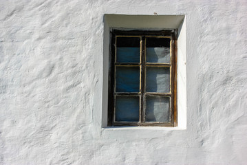 An old window against the background of a white clay house in the village in summer.