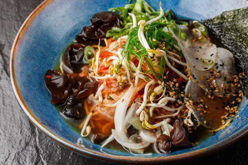 Asian vegetarian noodle soup, ramen with tofu, kimchi, vegetables and mushrooms in blue bowl. Slate background. Top view. Bowl of asian style soup. Japanese cuisine. Top view. Banner. Asian food