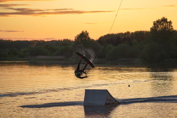 Wakeboarder making tricks. Low angle shot of man wakeboarding on a lake. Man water skiing at sunset.