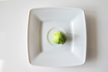 small green brussels sprouts on a white plate on a white isolated background