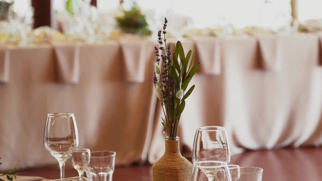 Wildflowers, lagurus and lavender stand in a glass vase on a festive table on a pink tablecloth near a glass goblet