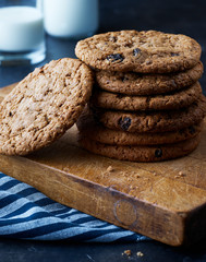 Fresh baked cookies on a wooden board. Cookie stack. Glass of milk, milk bottle on black background
