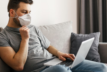 Young man with medical mask working home online at quarantine