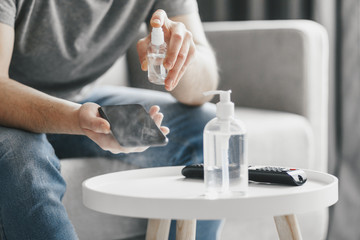 Man at home disinfecting hands and smartphone by sanitizer