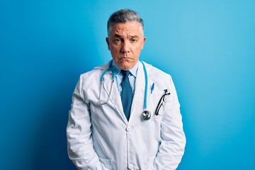 Middle age handsome grey-haired doctor man wearing coat and blue stethoscope depressed and worry for distress, crying angry and afraid. Sad expression.