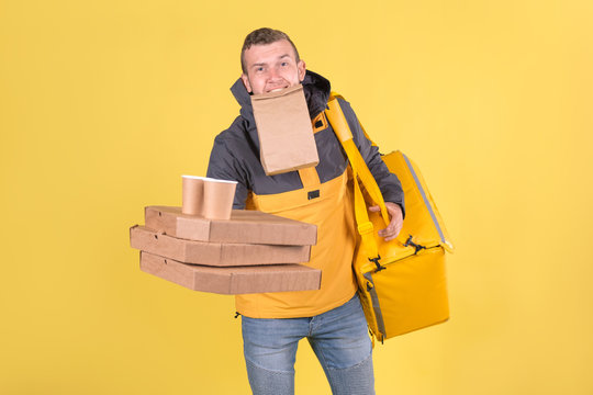 Portrait caucasian courier and food delivery young boy teenager in yellow uniform with thermo bag, offer forward an order with pizza and coffee cups in biodegradable eco-friendly packaging on yellow