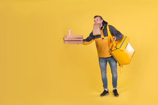 Portrait caucasian courier and food delivery young boy teenager in yellow uniform with thermo bag, offer forward an order with pizza and coffee cups in biodegradable eco-friendly packaging on yellow