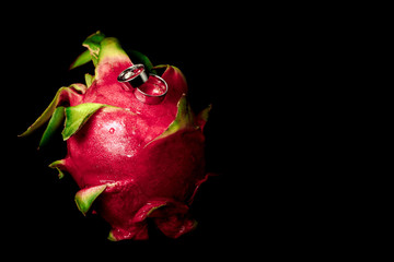 Wedding rings white gold on an exotic fruit - close-up, black background