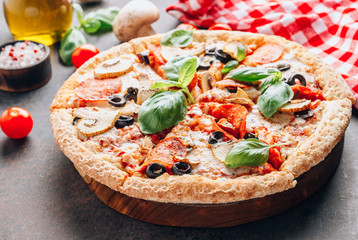 Sliced italian pizza with salami, mozzarella, mushroom, tomatoes, black olives and basil leaves on black background. Italian traditional food. Popular street food concept