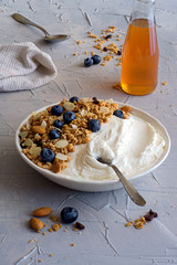 Healthy breakfast of natural yogurt with granola, nuts, almonds, blueberries and honey. Blueberries, granola, spoon, rag and bottle with honey on the table.