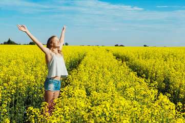 Happy girl with wide open hands in a yellow flowering field on a sunny day experiences a feeling of joy and freedom